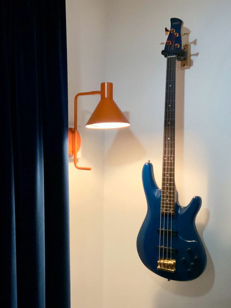 Bass guitar hanging on wall next to orange wall light