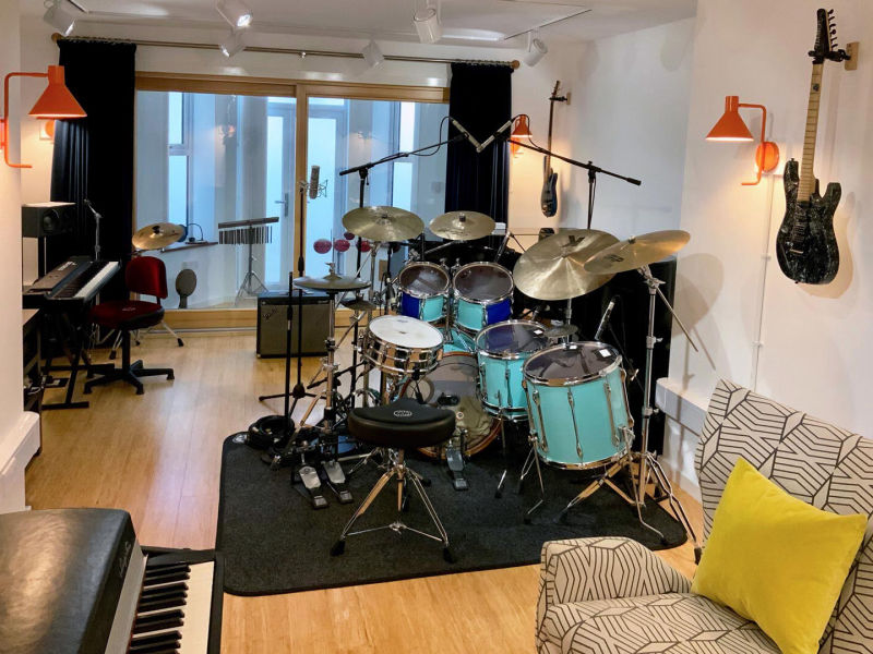 Basement recording studio with drum kit, grand piano, guitars, microphones, keyboard, monitor speakers, spot lights, Rhodes piano, acoustic doors and isolated recording bay