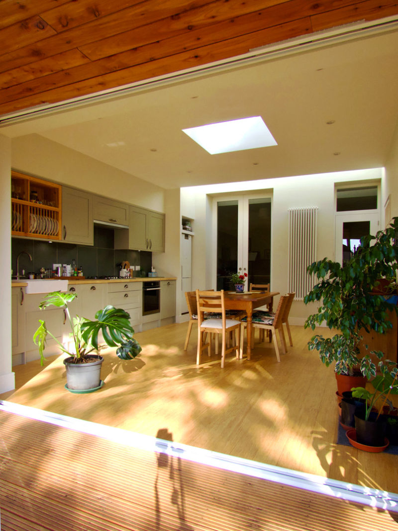 sun shining into modern kitchen extension with roof lights, column radiator, pocket doors and bamboo floor